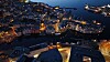 Oversikt over en opplyst Ålesund ved vannet i skumringen med båter og broer.