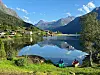 To små båter ved bredden av et rolig fjellvann med speilblankt vann og bratte fjell i bakgrunnen.