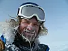 Nærbilde av en person med skibriller, snø i skjegg og hår, ute i vintervær.