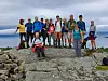 En gruppe turgjengere står og sitter på en steinete fjelltopp med utsikt mot skyet himmel.