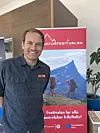 En smilende mann står ved siden av et rødt Naturfestivalen-banner med fjellmotiv.