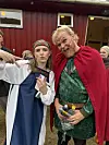To personer i historiske kostymer står foran en rød bygning og ser mot kamera.