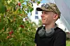 En mann med hodetelefoner rundt halsen står ved et bærtre med røde bær og grønne blader.