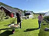 En person med trillebår står på en gressplen ved røde bygninger mens en annen går i nærheten.