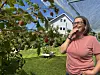 En kvinne står i en grønn hage ved et frukttre med røde frukter og et stort beskyttelsesnett.