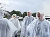 Fire personer i gjennomsiktige regnponchoer står ved en småbåthavn på en regntung dag.