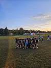 En gruppe unge fotballspillere poserer samlet på en gressbane i skumringen.