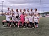 En gruppe fotballspillere i hvite drakter poserer på en kunstgressbane med en spiller i rosa keeperdrakt foran.