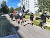 En gruppe fotballspillere og en voksen går langs en vei med et stort svart-hvitt flagg.