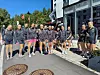 En gruppe ungdommer og voksne i svarte klubbklær står samlet foran en moderne bygning utendørs.