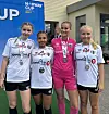 Fire fotballspillere i drakter og medaljer står foran et Norway Cup-skilt.