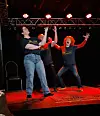 Tre personer står på en scene med rødt lys og svarte baktepper mens de spiller improvisasjonsteater.