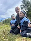 To barn og en voksen sitter på gresset ute på en eng.