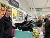 Kunder i en butikk står ved kassen mens varer og solformørkelsesbriller ligger utstilt.