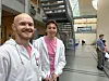 To smilende menn står i et atrium på et universitetsområde med trapper, glassvegger og noen personer i bakgrunnen.
