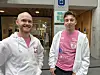 To menn i hvite hettejakker og rosa T-skjorter står foran en bygning med NTNU-skilt.