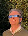 Mann utendørs med briller for solformørkelse, vendt oppover mot solen.