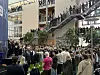 En stor folkemengde står samlet i et innendørs atrium med rulletrapp og åpne balkonger.