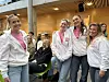 Fire kvinner står tett sammen og smiler foran en inngang med glass og trepanel.