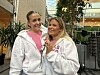 To kvinner i hvite hettegensere står tett sammen innendørs og smiler.