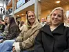 Tre kvinner sitter på en tribune i en innendørs hall.