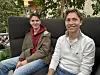 To ungdommer sitter på en sofa i et lyst innemiljø.