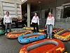 Tre studenter står blant flere fargerike oppblåsbare båter foran en bygning.