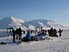 En gruppe mennesker står og sitter på snødekt mark med stativ og kameraer foran snødekte fjell.
