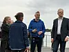 Fire personer står ute ved en kai med vann og overskyet himmel i bakgrunnen.