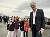 En mann i dress står ved siden av fire barn utendørs i overskyet vær.