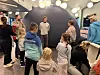 Flere personer står samlet rundt en stor mørk kuppel i et innendørs utstillingsrom.