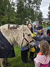 Ponni med lang man står blant barn og voksne i en park.