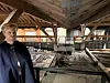 En person står i et skadet, forlatt bygg med eksponerte bjelker og ødelagt gulv.