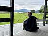 Person sitter på en veranda med utsikt mot grønt landskap, vann og fjell.