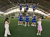 Cheerleadere trener løft og pyramider i en innendørshall mens to personer ser på.
