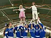 Barn løftes av et cheerleadinglag i en innendørs hall.