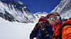 To personer tar en selfie med snødekte fjell og isbreer i bakgrunnen.
