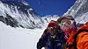 To personer tar en selfie med snødekte fjell og isbreer i bakgrunnen.