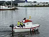 En liten rød og hvit båt med flere passasjerer seiler på rolig vann i en havn.