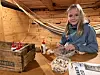 Et barn sitter ved et bord i en trebåt med en bolle og flasker, mens et annet barn henger i en køye i bakgrunnen.