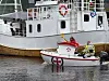En liten rød og hvit Eliasbåt ligger ved siden av et større hvitt fartøy i havna.