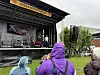 Folk i regntøy ser mot en utendørsscene med Trebåtfestival-skilt i en havn.
