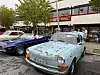 Flere veteranbiler står parkert foran bygninger langs en gate, med folk i bakgrunnen.