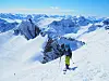 En skikledt person går på en smal snørygg med fjelltopper i bakgrunnen.