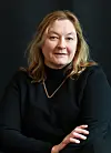 Portrett av en kvinne med lyst hår i svart genser foran mørk bakgrunn.