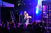 Et band spiller på en utendørsscene foran publikum, opplyst av blått og lilla lys.