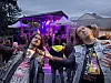 To publikummere står foran en opplyst utendørsscene med flere konserttilskuere i bakgrunnen.