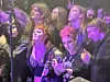 Tett publikum i mørke klær står foran en konsertscene med lilla lys.