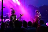 Et band spiller på scene med lilla lys, mens publikum står i silhuett foran.