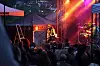 Et rockeband spiller på en utendørsscene foran et tett publikum i skumring.